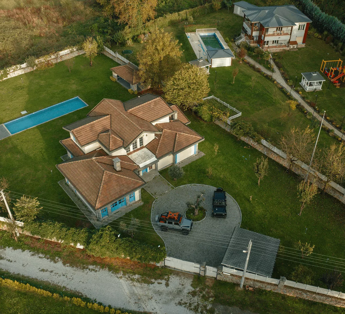Aerial drone view of a large estate with a tile-roof villa, swimming pool, manicured lawns, and perimeter fencing.