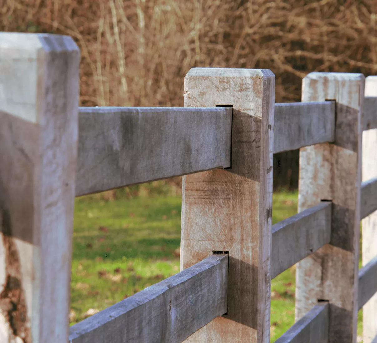 Close-up of a weathered gray wooden split-rail fence post with horizontal boards slotted through on a green lawn.